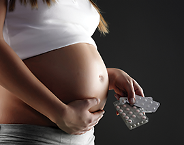A pregnant woman with one hand on her belly and the other hand holding a packet of pills. 