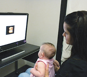 Mother holding baby on her lap, sitting in front of computer screen, being tested for oculomotor functioning. 