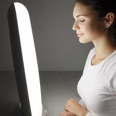 Photo: Seated woman in front of light therapy device.