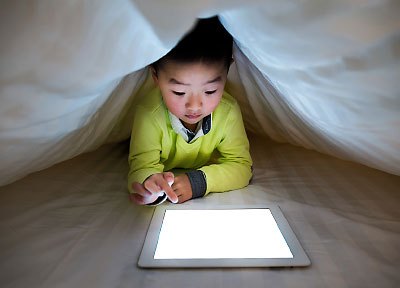 Photo: child looking at tablet under blanket