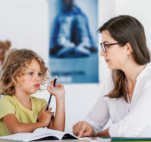 Photo: Lady with Glasses looking at a child holding a pencil in front of an open book