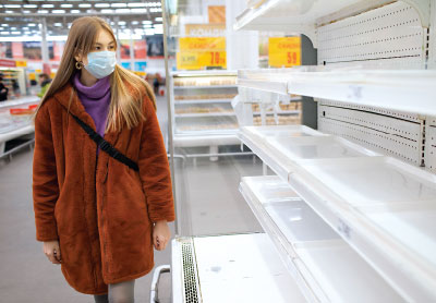 Photo: Lady wearing mask looks at empty shelves in a supermarket