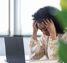 Photo: young woman holding her head in front of a laptop