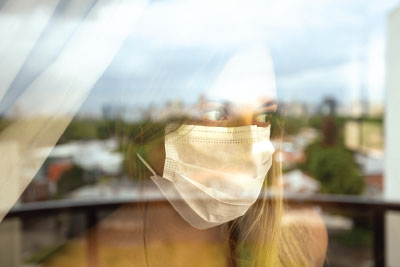 Photo: Lady wearing a mask looking outside a window