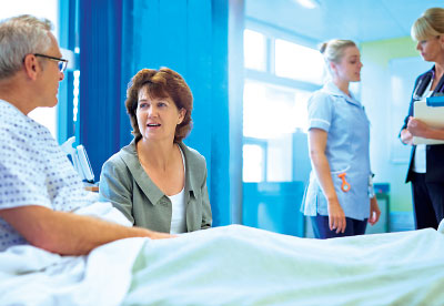 Photo: Patient in bed talking with a lady and nurse and otehr professional talking in the background.