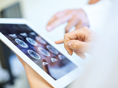 Photo: hands operating on a tablet with brain scan images