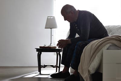 Photo: older person sitting on the side of a bed looking pensive
