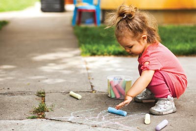 Photo: Child playing with some colored chalk on a sidewalk