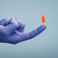 Photo: gloved hand and orange pill