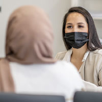 Woman wearing PPE and talking with woman wearing a hijab