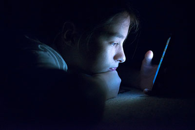 Photo: young person looking at a phone in the darkness