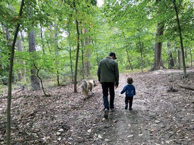 Photo of a father and daughter and their dog walking on a path in a forest.