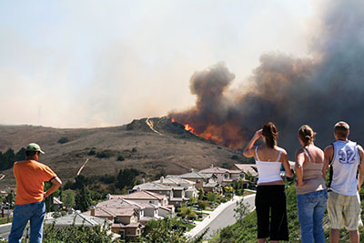 Photo of people watching a wildfire at a distance that is close to a row of houses.
