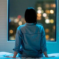 Image of a woman sitting on a bed looking out of a window