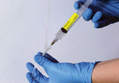 Photo of gloved hands injecting a syringe of Ketamine into an IV injection port.