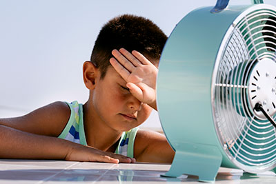 Photo of a young boy in front of a fan on a hot day.